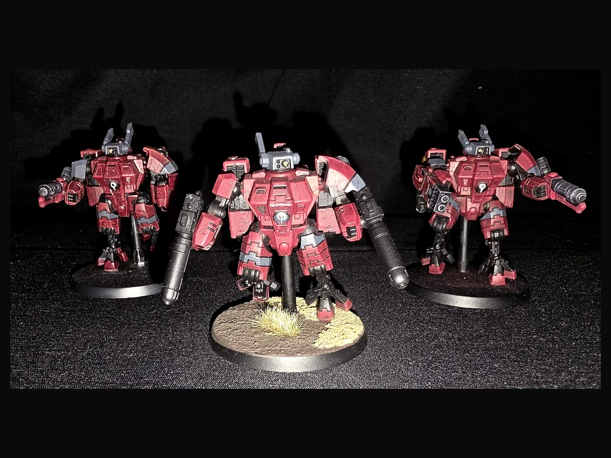 Group of painted red T’au battlesuit miniatures.